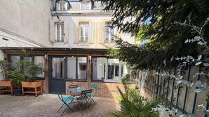 Une cour avec une table et des chaises, des plantes en pot et un mur en briques.