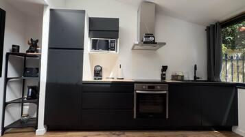 A modern kitchen with black cabinetry, a built-in oven, a microwave, and a coffee maker.