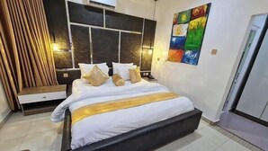 Ett modernt hotellrum med en stor säng, ett sängbord, en liten avlastningsyta, en väggmonterad luftkonditioneringsanläggning och en färgstark, abstrakt tavla.