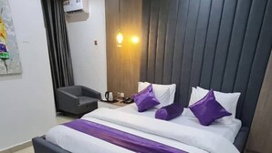 Ett modernt hotellrum med en stor säng, ett sängbord, en luftkonditioneringsanläggning och en väggmonterad lampa.