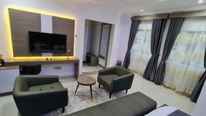 Ett modernt hotellrum med en stor säng, två fåtöljer, ett litet bord, en tv och en spegel.