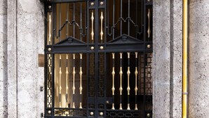 A black metal gate with vertical bars and decorative elements, set against a textured stone wall.