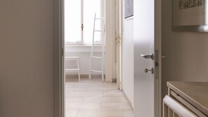A hallway with a white door, a window, and a white ladder leaning against the wall.