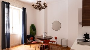 A dining area with a round table, four chairs, a chandelier, a potted plant, and a mirror on the wall.
