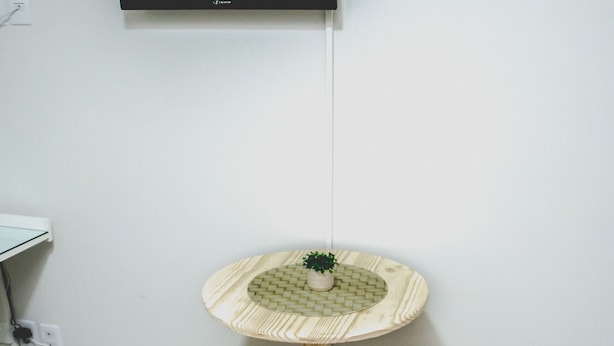 A small wooden table with a woven top and two matching stools. A flat-screen TV is mounted on the wall above the table. - Tima Kitnet Prox Unifei com Wi-fi e Smart TV (Itajuba)