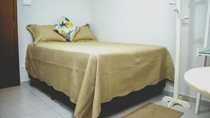 A small, neatly made bed with a beige bedspread and a decorative pillow. - Tima Kitnet Prox Unifei com Wi-fi e Smart TV (Itajuba)