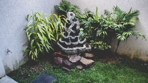 A garden with a rock sculpture, various plants, and a small pond. - Tima Kitnet Prox Unifei com Wi-fi e Smart TV (Itajuba)