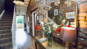 A staircase with a patterned carpet, a stone wall, a mirror, a lamp, and a vase with flowers.