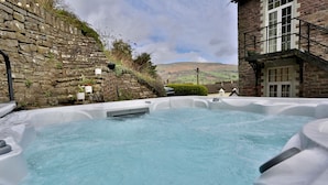 A hot tub with a stone wall and a building in the background.