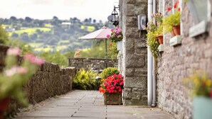 A stone building with flower boxes and a pathway leading to a table and umbrella.