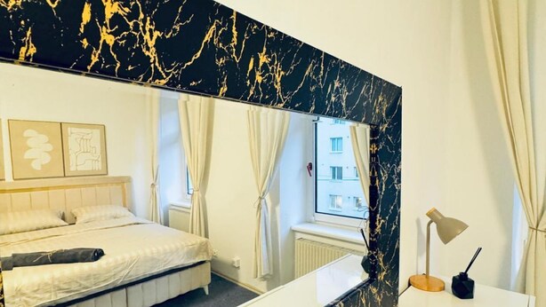 Een hotelkamer met een bed, een grote spiegel, een bureau met een lamp en uitzicht op een gebouw.