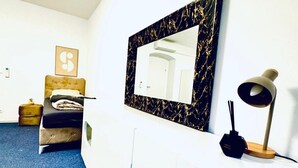 Een hotelkamer met een bed, een nachtkastje met lamp, een spiegel met zwarte marmeren lijst en een ingelijst schilderij aan de muur.