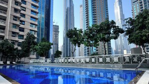 A swimming pool with a checkered pattern, surrounded by high-rise buildings and trees. - SIMPLY COMFORT Luxury Burj Khalifa & Fountain View Apartments Steps to Dubai Mall (Dubai)
