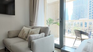 A modern living room with a grey sofa, a small table, and a balcony with a chair. - SIMPLY COMFORT Luxury Burj Khalifa & Fountain View Apartments Steps to Dubai Mall (Dubai)