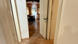 A hallway with a tiled floor leading to a dining area with a table and chairs. - Just steps from Cala D'Ambra beach and the center of San Teodoro, we offer a practical, air-conditioned three-room apartment for 4-6 people, with acourtyard and outdoor parking space. The apartment features a living room with a sofa bed and TV, a fully e (San Teodoro)