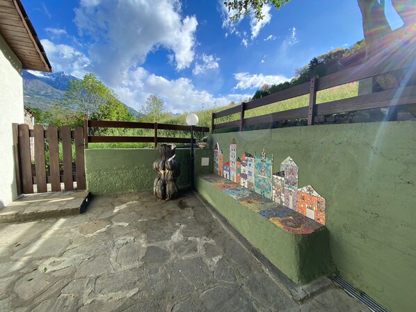 A stone-paved entrance with a wooden fence, a mosaic wall, and a view of mountains. - Large lodge in the Park, with garden and Elf house. (morbegno)