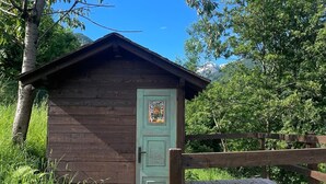 Eine kleine Holzhütte mit grüner Tür, umgeben von üppigem Grün und einer Holzterrasse.