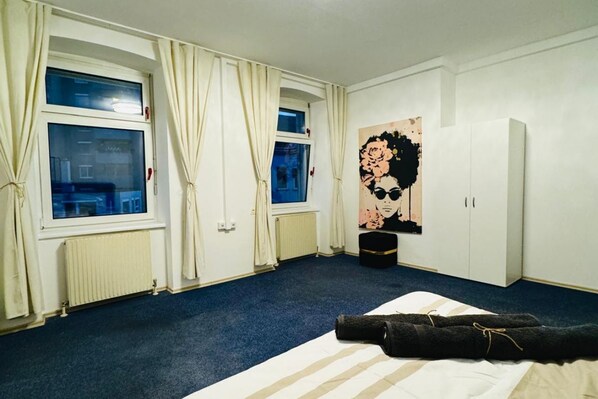 A hotel room with a bed, a radiator, a window with curtains, a poster on the wall, and a wardrobe.