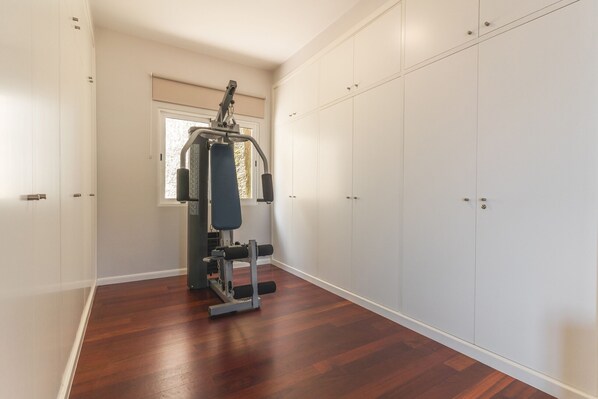 A room with a wooden floor, a window, and a wall-mounted exercise machine.