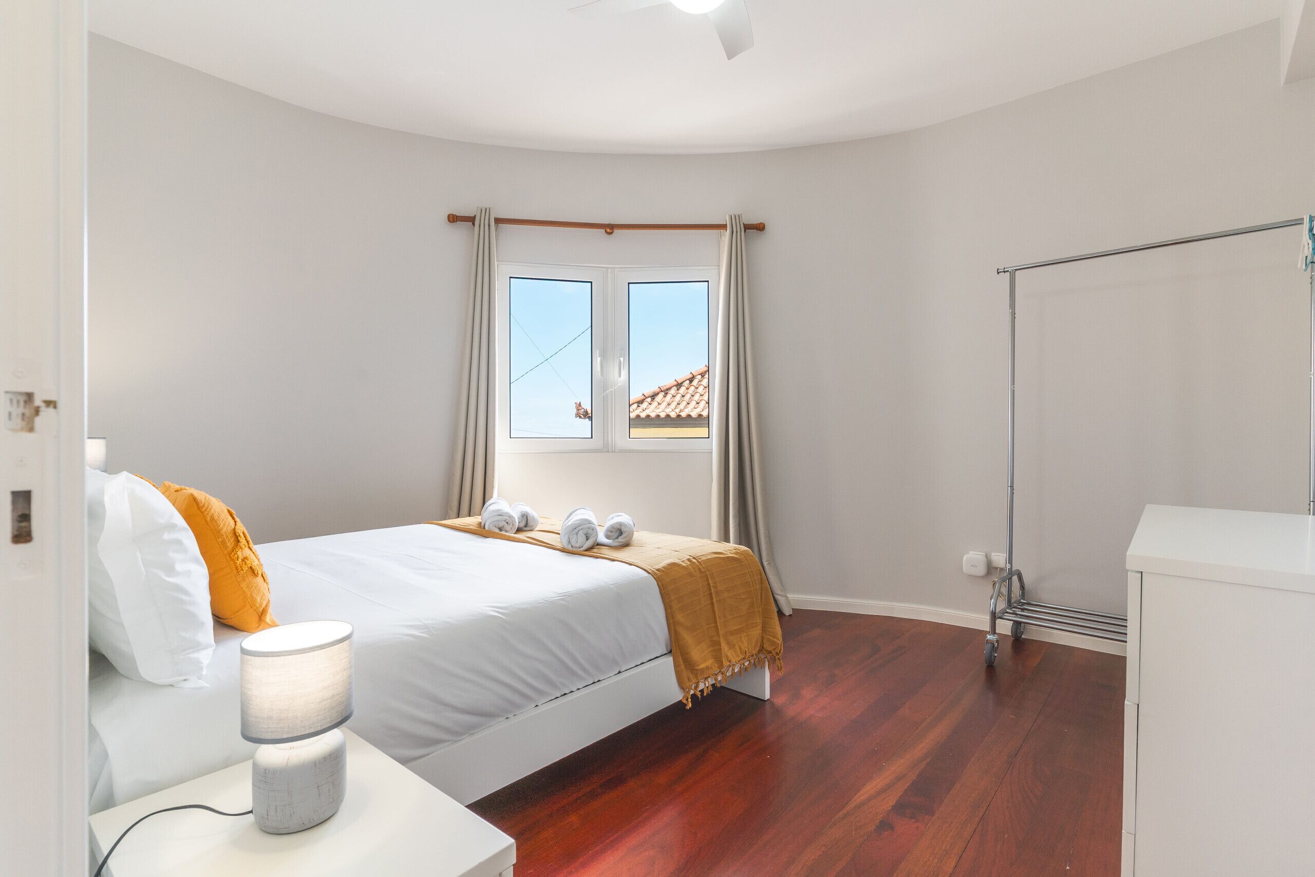 A bedroom with a bed, a bedside table, a lamp, a window with curtains, and a radiator.
