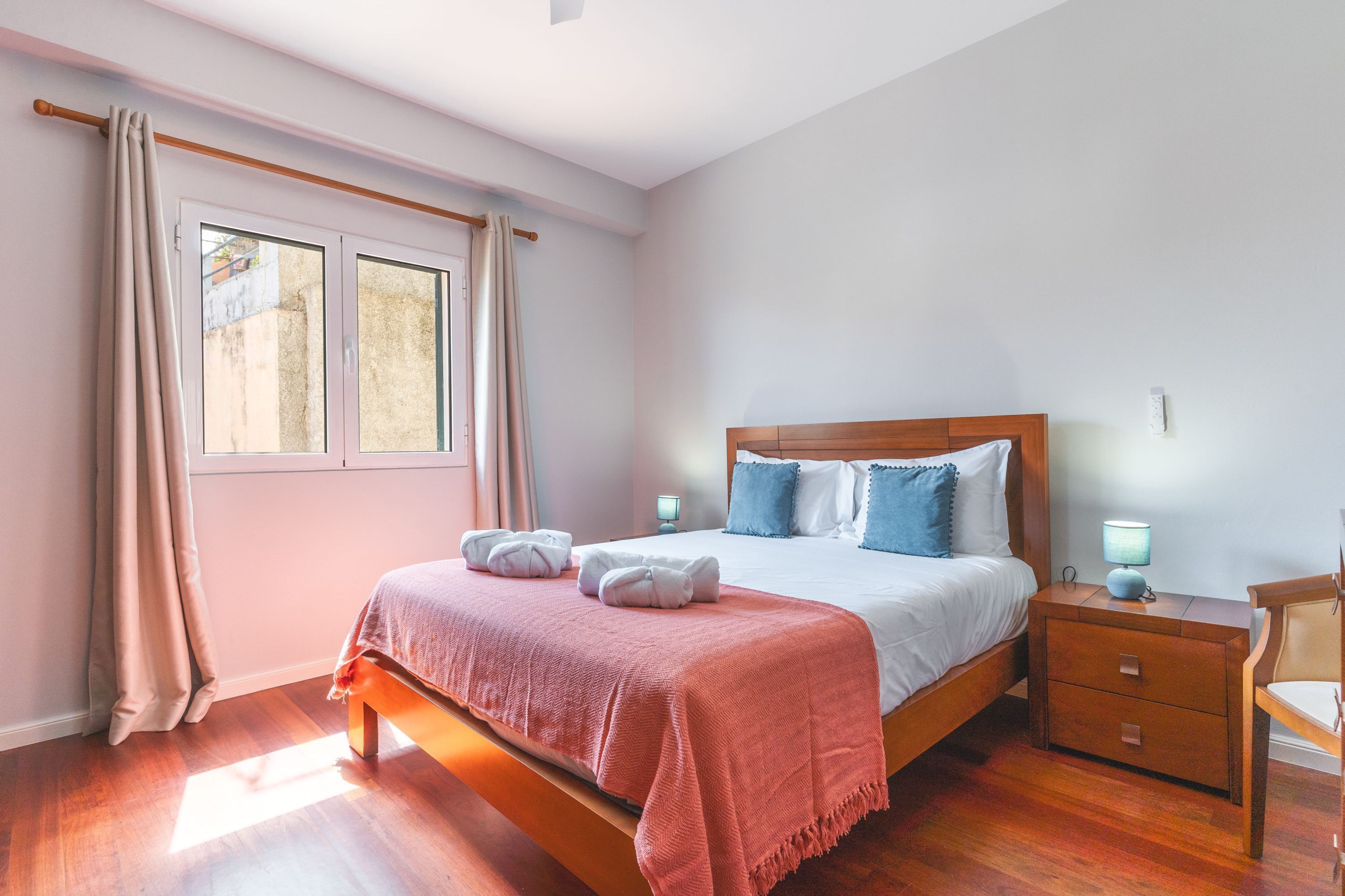 Ein Schlafzimmer mit einem Holzbett, einem Nachttisch, einem Beistelltisch und einem Fenster mit Vorhängen.
