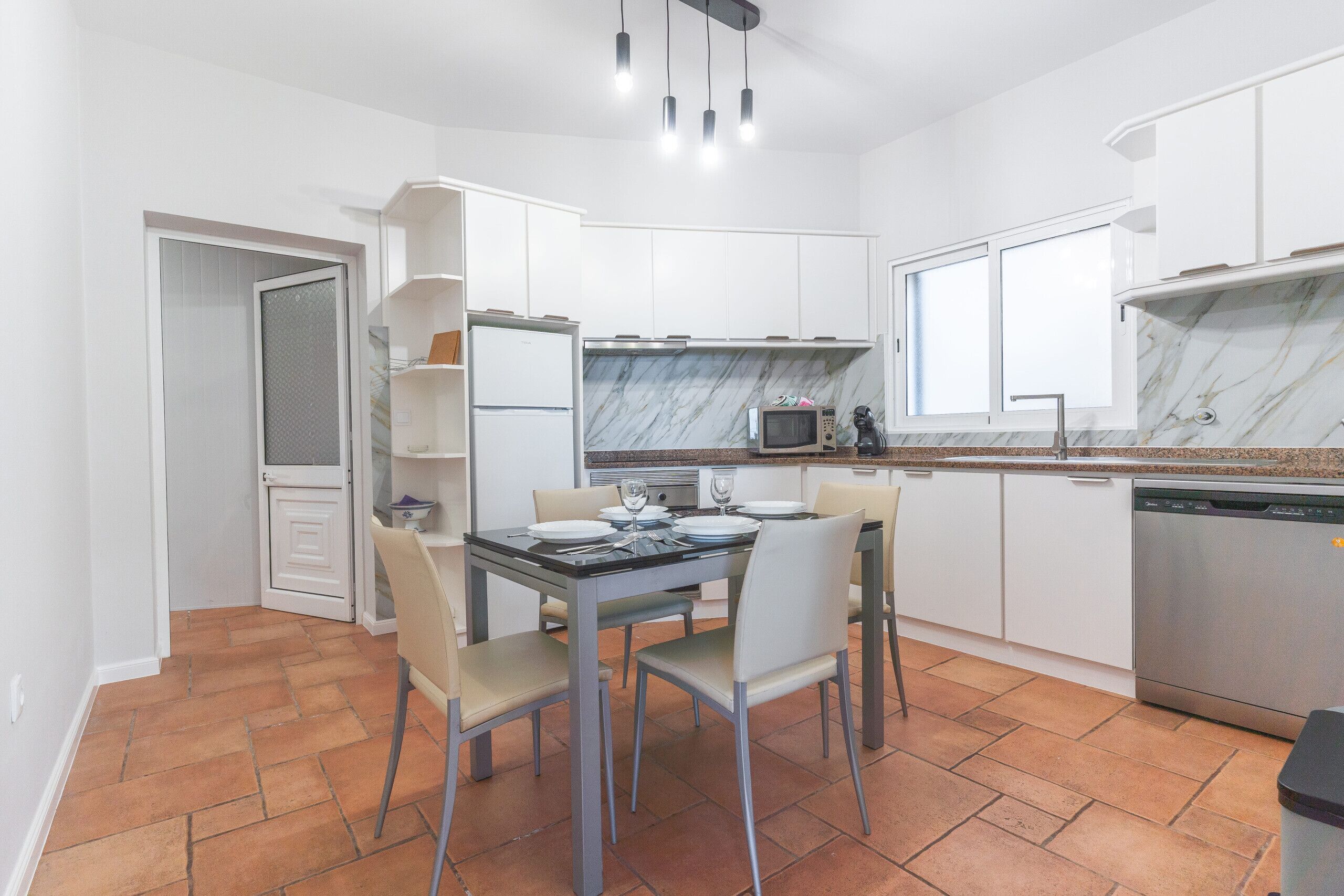A modern kitchen with white cabinets, a marble backsplash, and a dining area with a table and chairs.