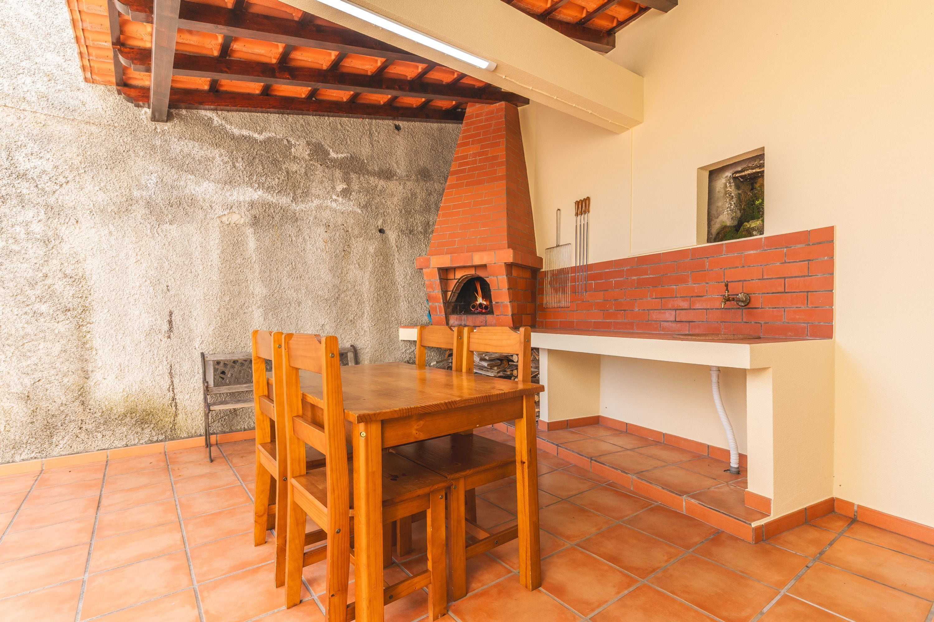 A patio with a brick oven, wooden table, and chairs.