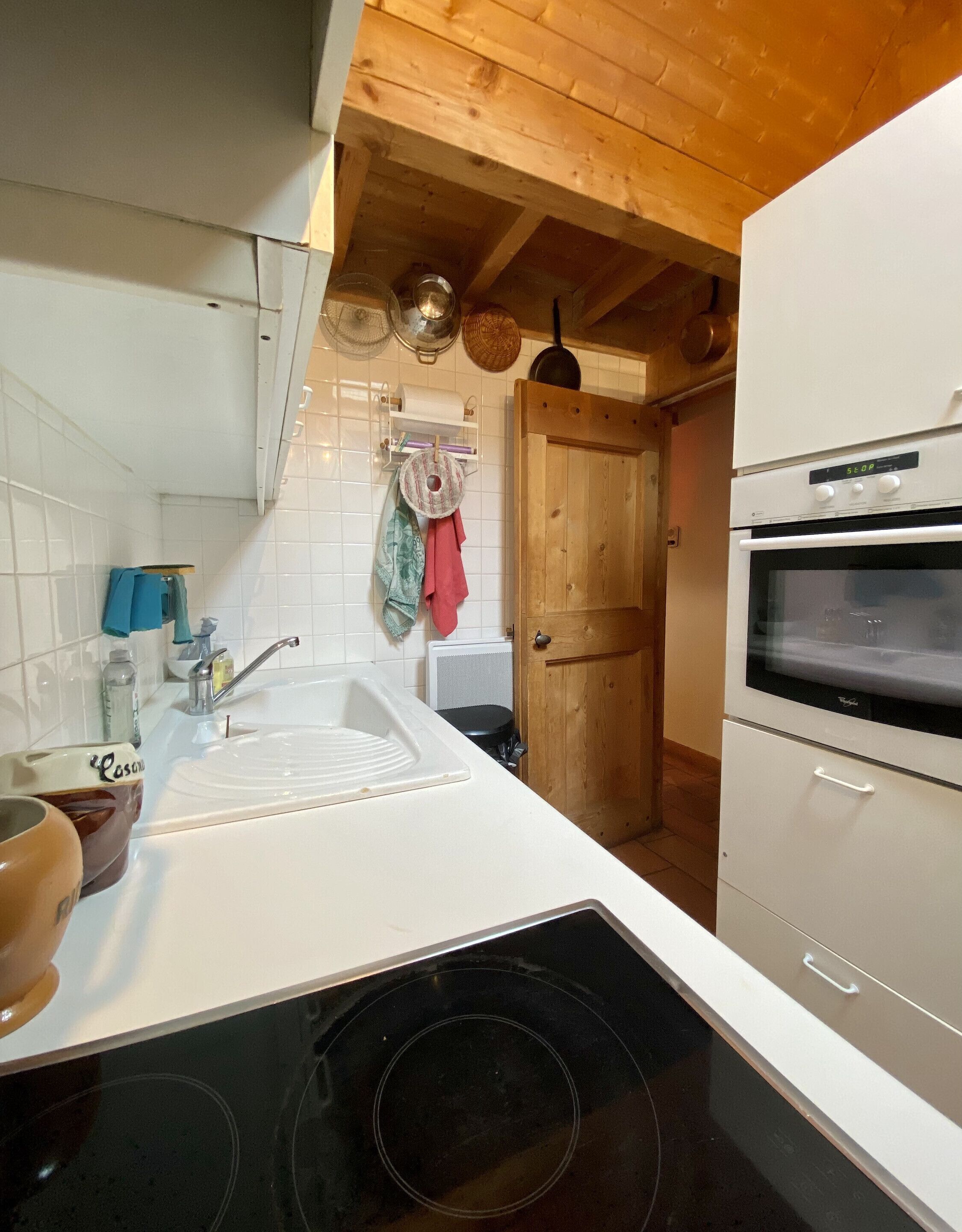 Una cocina con encimera blanca, fregadero, estufa y vigas de madera en el techo.