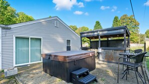 Un bain à remous avec des marches, un espace salon couvert et une maison avec un garage.