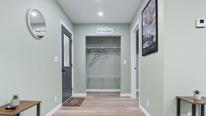 Un couloir avec un plancher en bois, un placard à manteaux, un miroir et une pancarte indiquant « Soyez les bienvenus ».