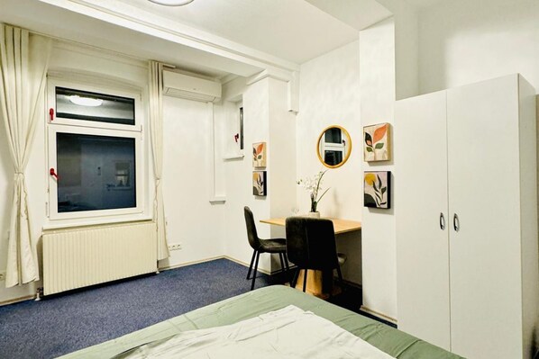 A hotel room with a bed, a desk, a chair, a wardrobe, a window with curtains, and wall art.