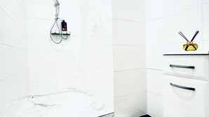 Un baño con azulejos blancos, una ducha y un estante pequeño con un objeto amarillo.