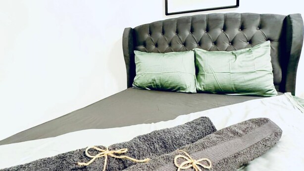 Una cama con cabecera capitonada, dos almohadas y una colcha.