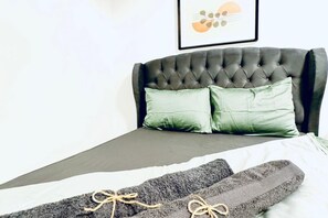 Un lit avec une tête de lit capitonnée, deux oreillers et une couverture.