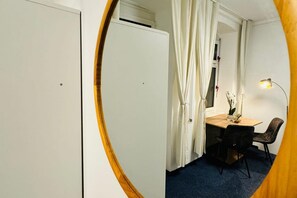 A room with a closed door, a window with curtains, a table with chairs, and a lamp.