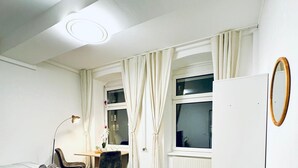Una habitación con cama, escritorio, silla, lámpara y ventana con cortinas.