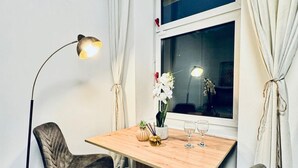 Un comedor con una mesa de madera, dos sillas, una lámpara de pie y un ventanal con cortinas.