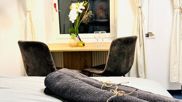 Una habitación de hotel con una cama, un escritorio con dos sillas, un jarrón con flores y una ventana con cortinas.