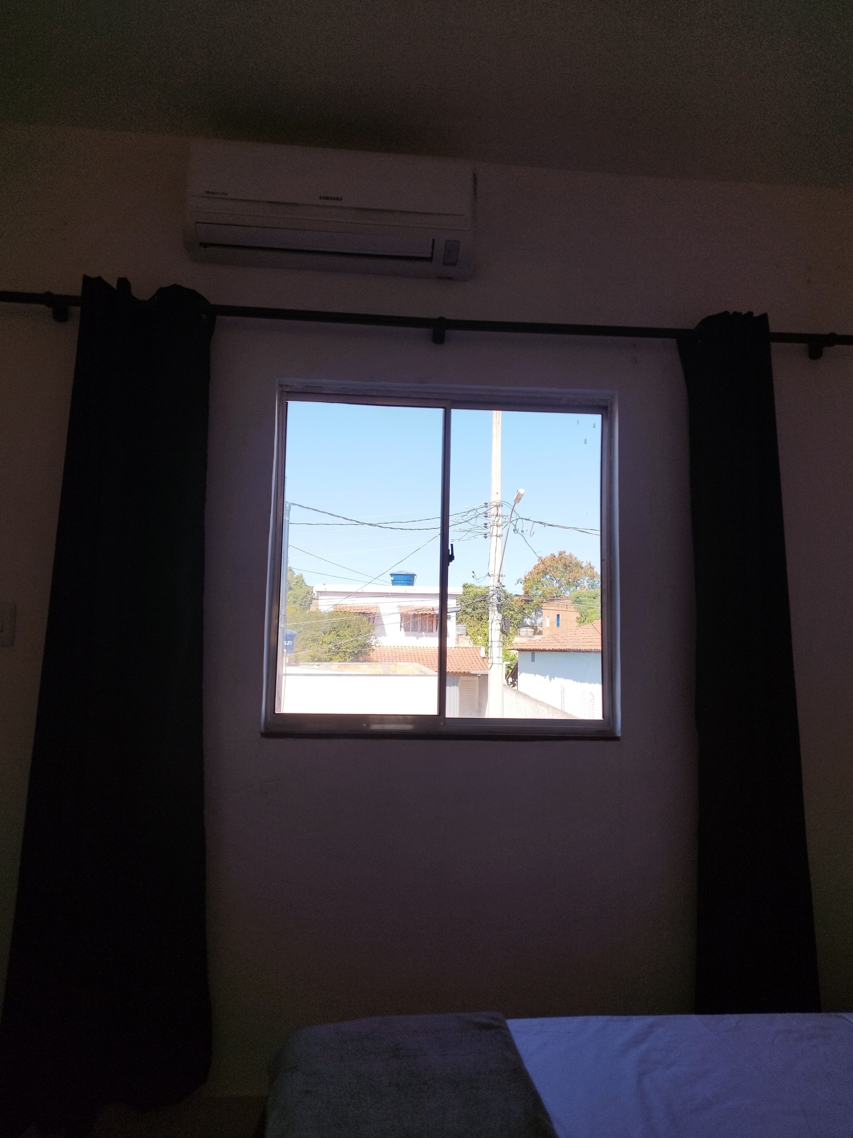 Une pièce dotée d’une grande fenêtre, d’un climatiseur placé juste au-dessus et d’un lit adossé au mur.