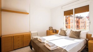 A bedroom with a large bed, wooden furniture, a nightstand, a window with a city view, and a picture frame on the nightstand. - Apartment in Gracia A34PAA1127 (Barcelona)