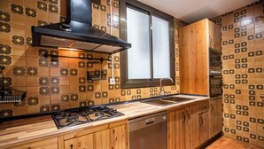 A kitchen with patterned tiles, wooden cabinets, a gas stove, a dishwasher, and a window with blinds. - Apartment in Gracia A34PAA1127 (Barcelona)