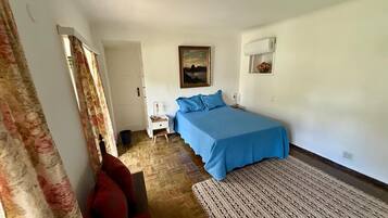 Een slaapkamer met een bed, nachtkastje, rode stoel, een kamerbreed tapijt en een schilderij aan de muur.