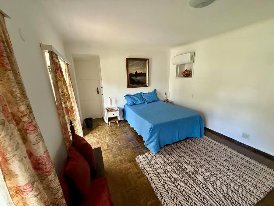 Een slaapkamer met een bed, nachtkastje, rode stoel, een kamerbreed tapijt en een schilderij aan de muur.