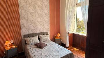 Une chambre avec un grand lit, un plancher en bois, un mur décoré d’un motif imitant le marbre et une fenêtre avec des rideaux.
