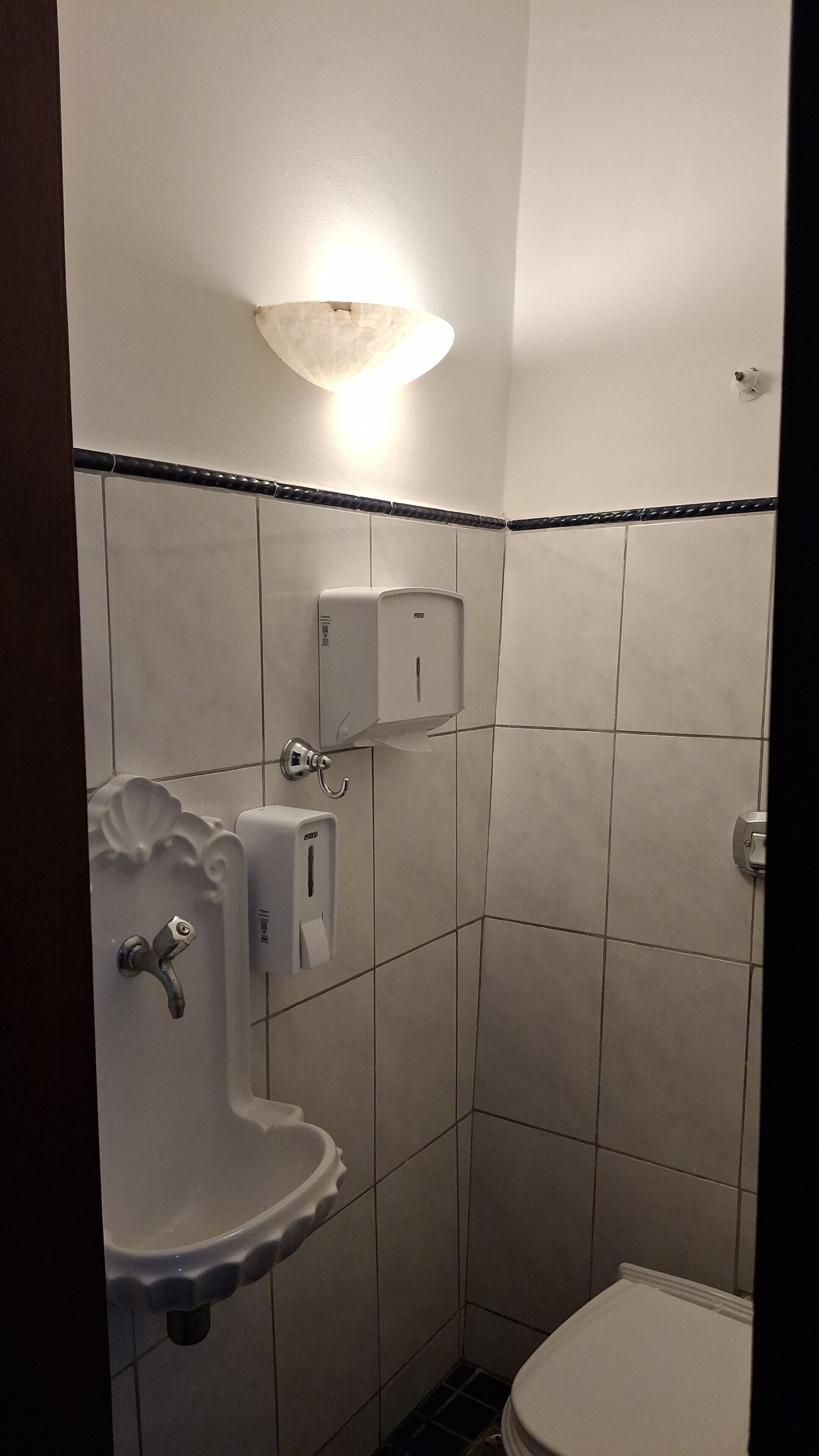 Un baño pequeño con revestimiento de azulejos, un lavamanos blanco, un inodoro y un secamanos.