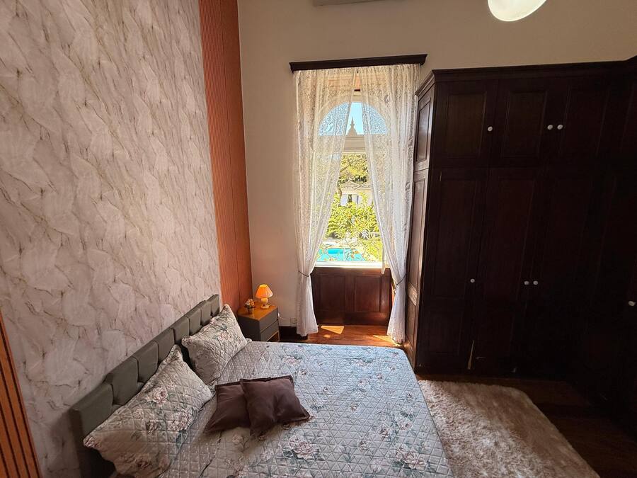Une chambre à coucher avec un lit, une table de chevet, une fenêtre avec des rideaux et une armoire.