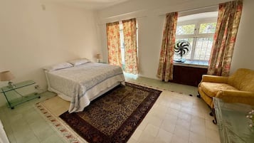 Un dormitorio con cama, una silla, una mesita y una ventana con cortinas.
