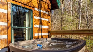 Una cabaña de madera con un jacuzzi en una terraza, rodeada de árboles.