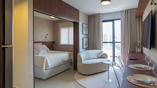 A modern hotel room with a bed, a seating area, a dining table with plates and glasses, and a TV mounted on the wall. - Apto no Butant c Academia e pr Ximo ao Metr (São Paulo)