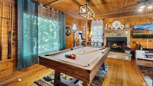 Um quarto acolhedor com mesa de bilhar, piso de madeira, lareira e televisão.